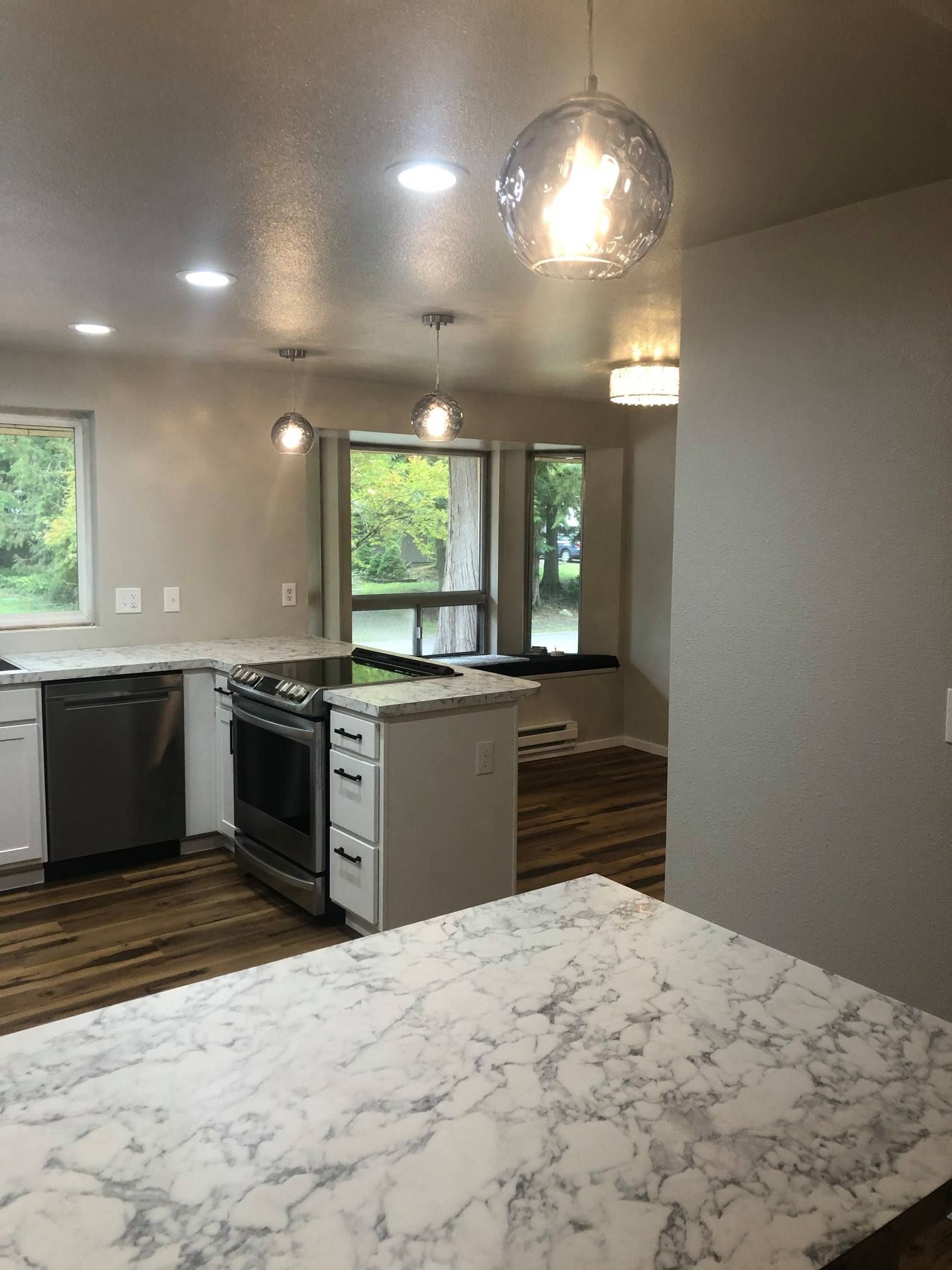 Modern kitchen with marble countertop island, stainless steel appliances, and pendant lights.