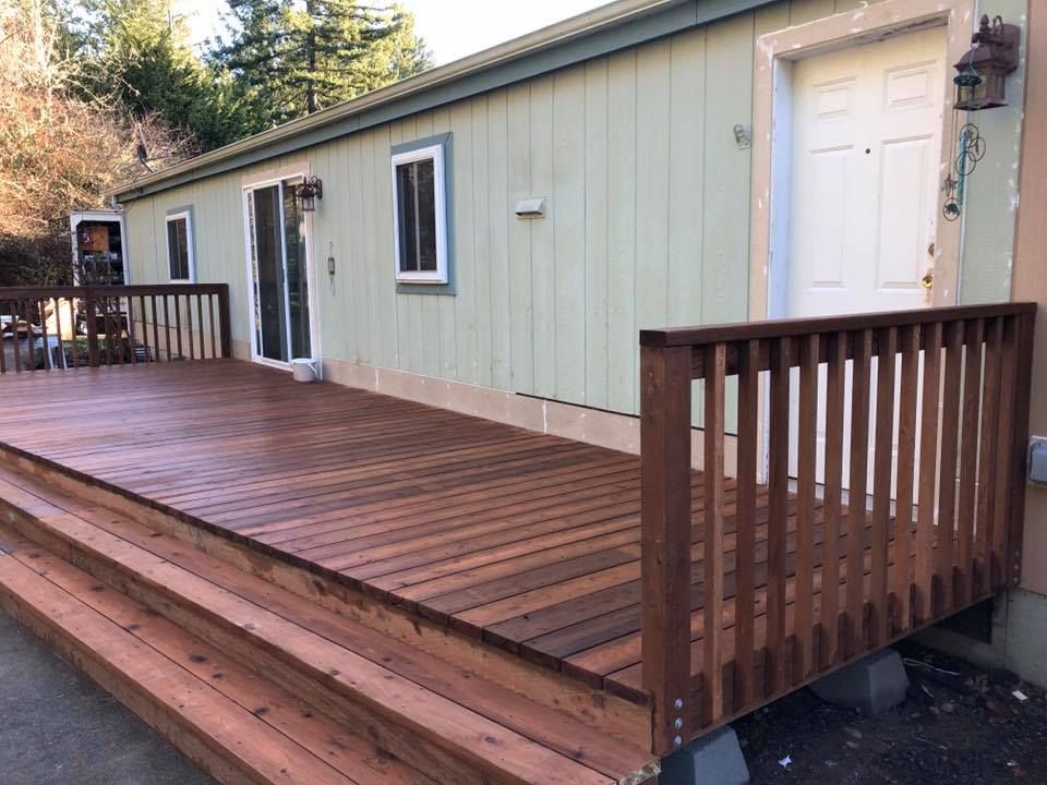 Wooden deck with steps in front of a light green house with white door and window.