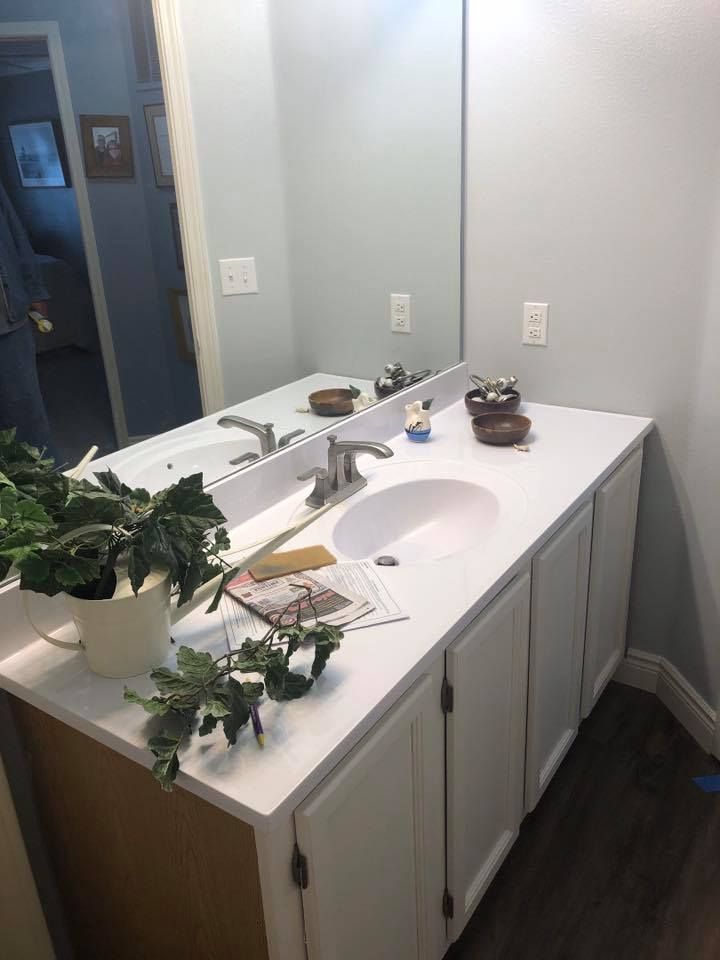 Bathroom vanity with a white countertop and cabinet doors, large mirror, and a single sink.