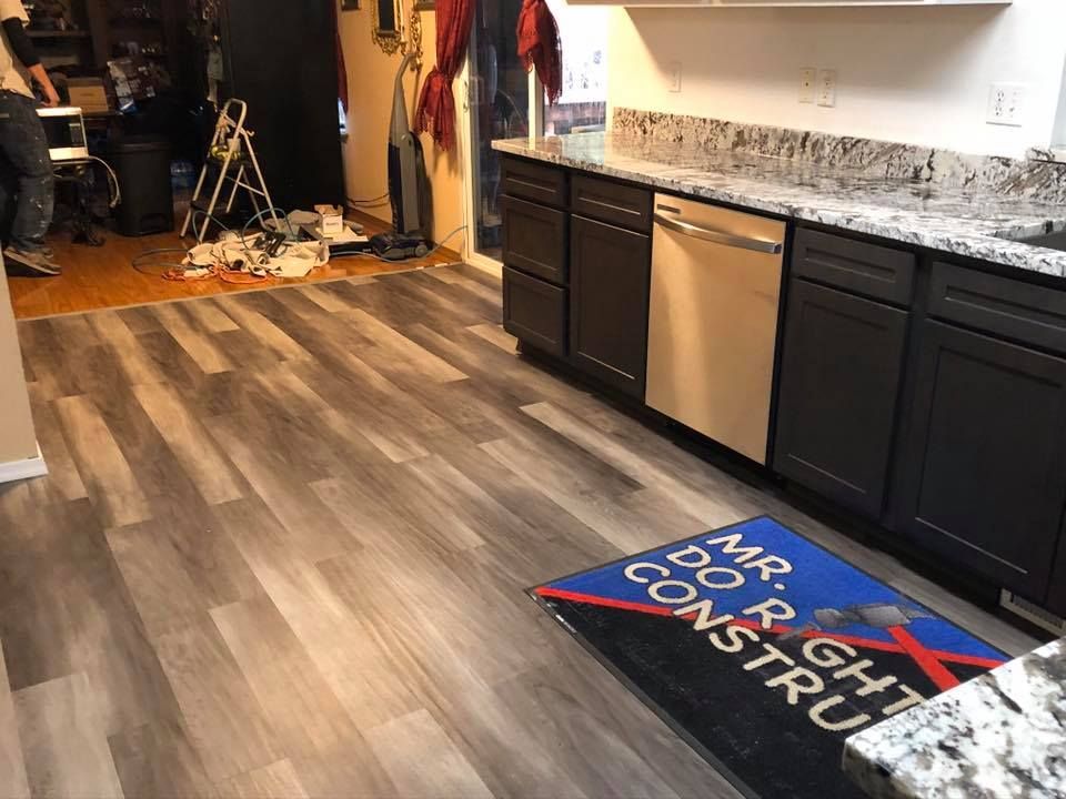 Kitchen with dark cabinets, light countertops, and gray wood-look flooring. A dishwasher is present.  