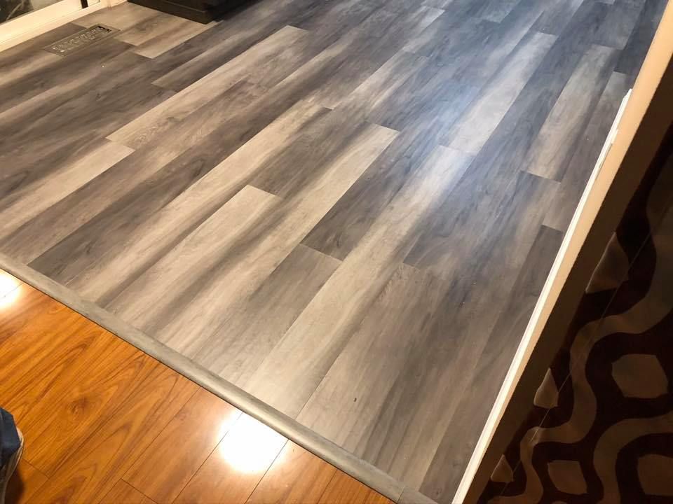 Gray wood-look flooring transitions to light brown wood and dark patterned rug.