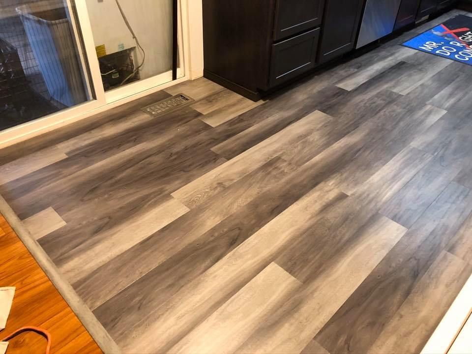 Gray wood-look flooring installed in a kitchen, next to a dark cabinet and a sliding glass door.