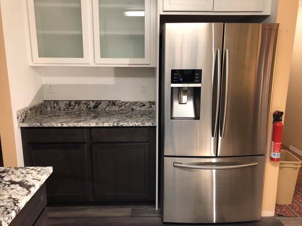 Kitchen with stainless steel refrigerator, dark cabinets, granite countertops, and white upper cabinets.