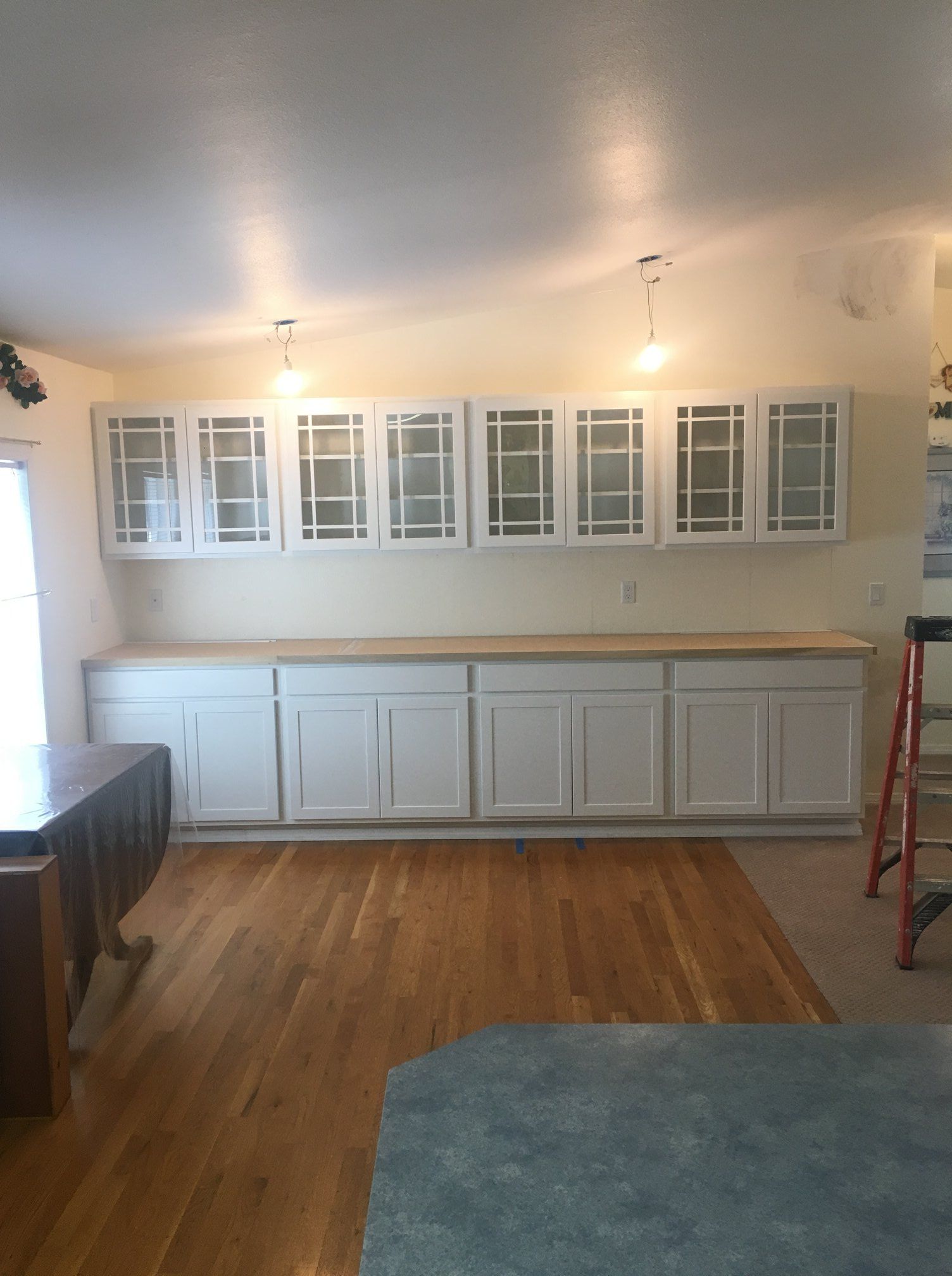 White kitchen cabinets along a wall; wooden countertop; hardwood floor.