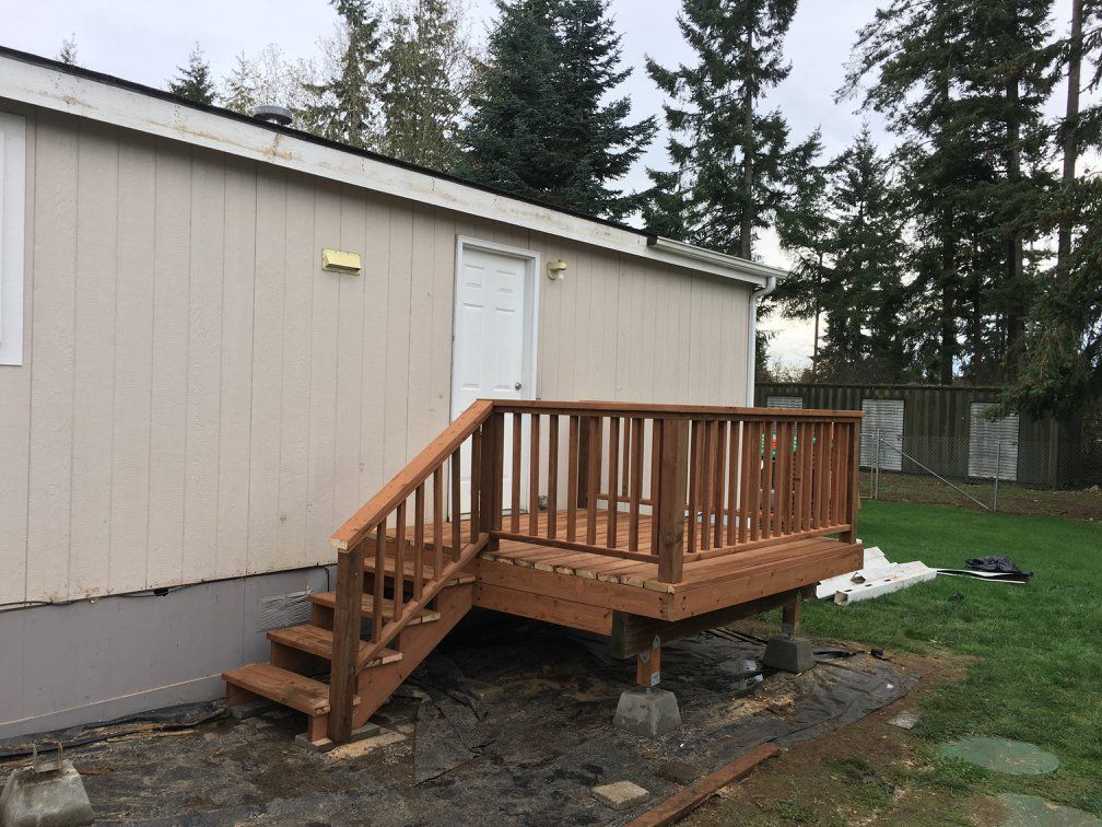 A wooden deck with stairs attached to the side of a beige mobile home.