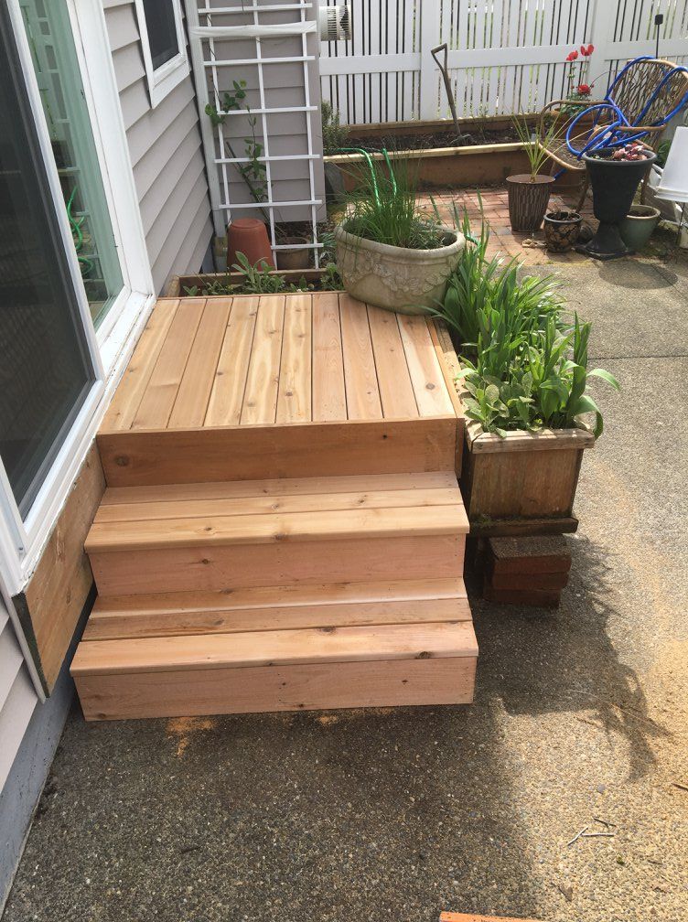 Wooden deck with three steps attached to a house; potted plants nearby.