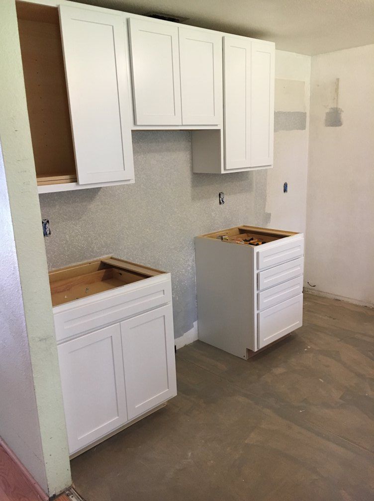 White kitchen cabinets in various stages of installation against a gray textured wall.
