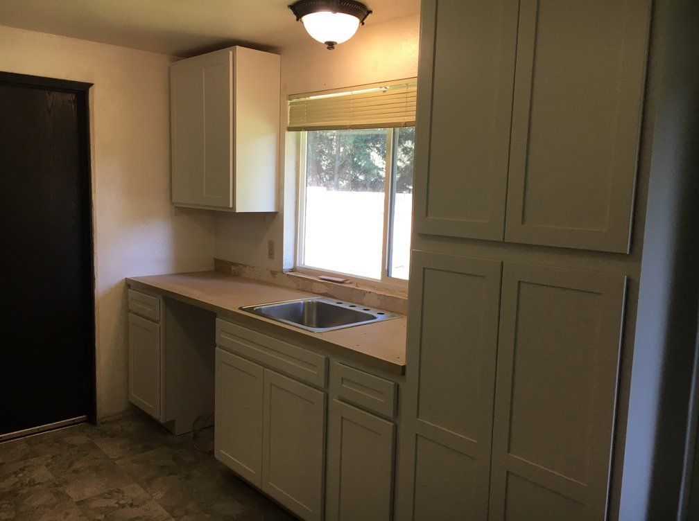 Small, white kitchen with cabinets, sink, and window.