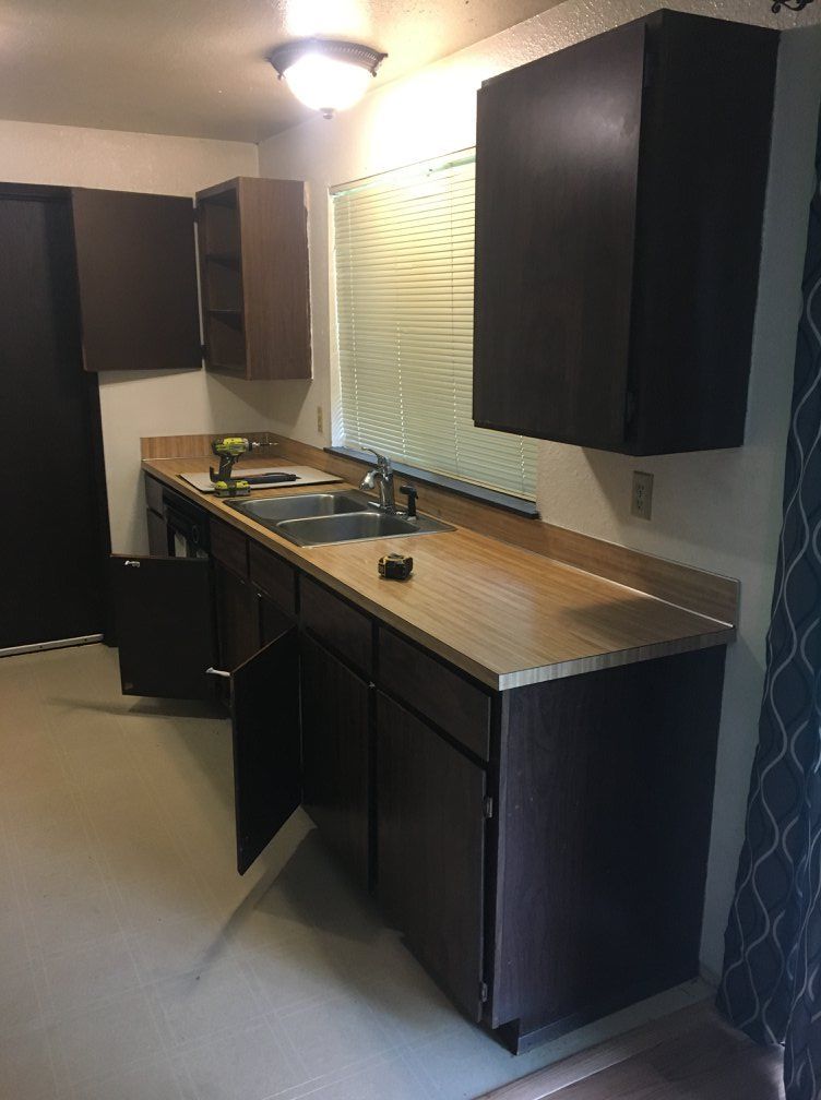 Kitchen with brown cabinets, light-colored countertops, and a window with blinds.