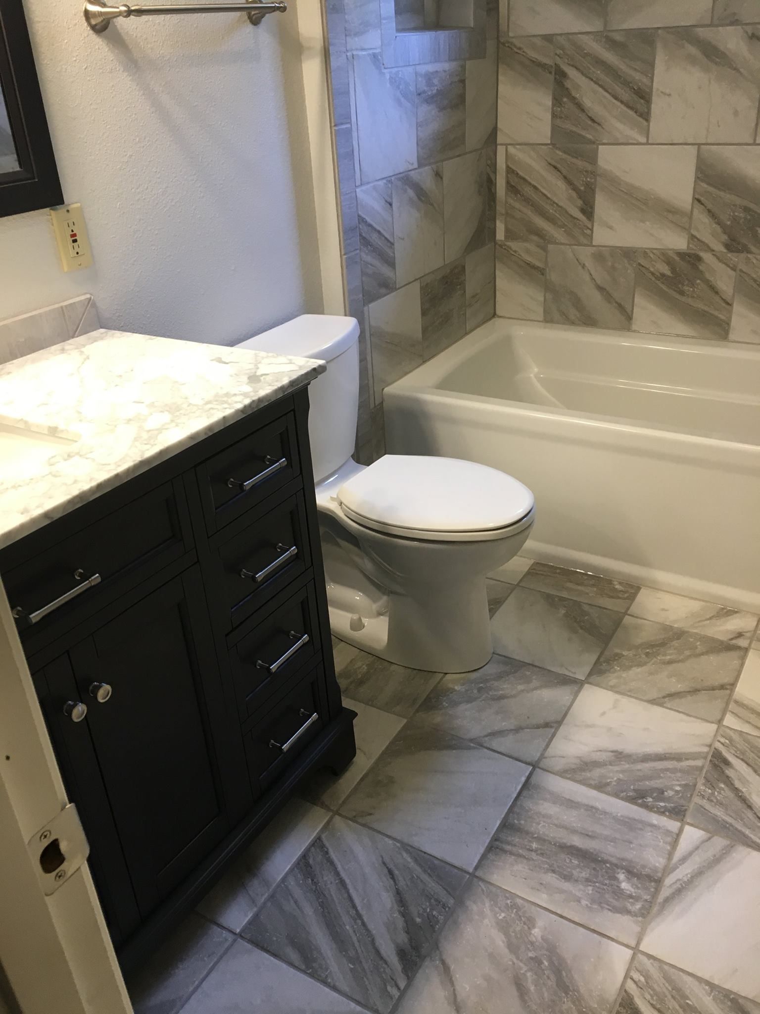 Bathroom with black vanity, white toilet, and gray tiled walls and floor.