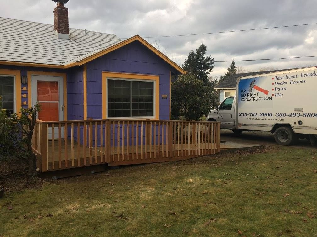 Purple house with wooden ramp, orange door, and a moving truck in front.