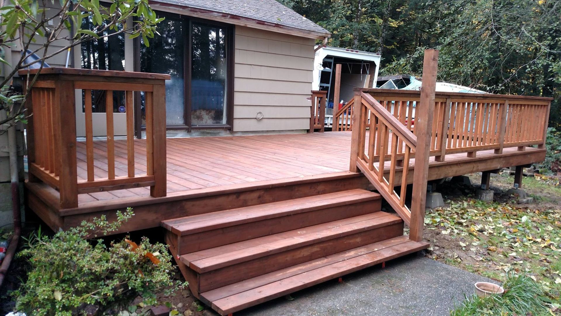 Wooden deck with steps and railing, stained brown, attached to a house with a sliding glass door.