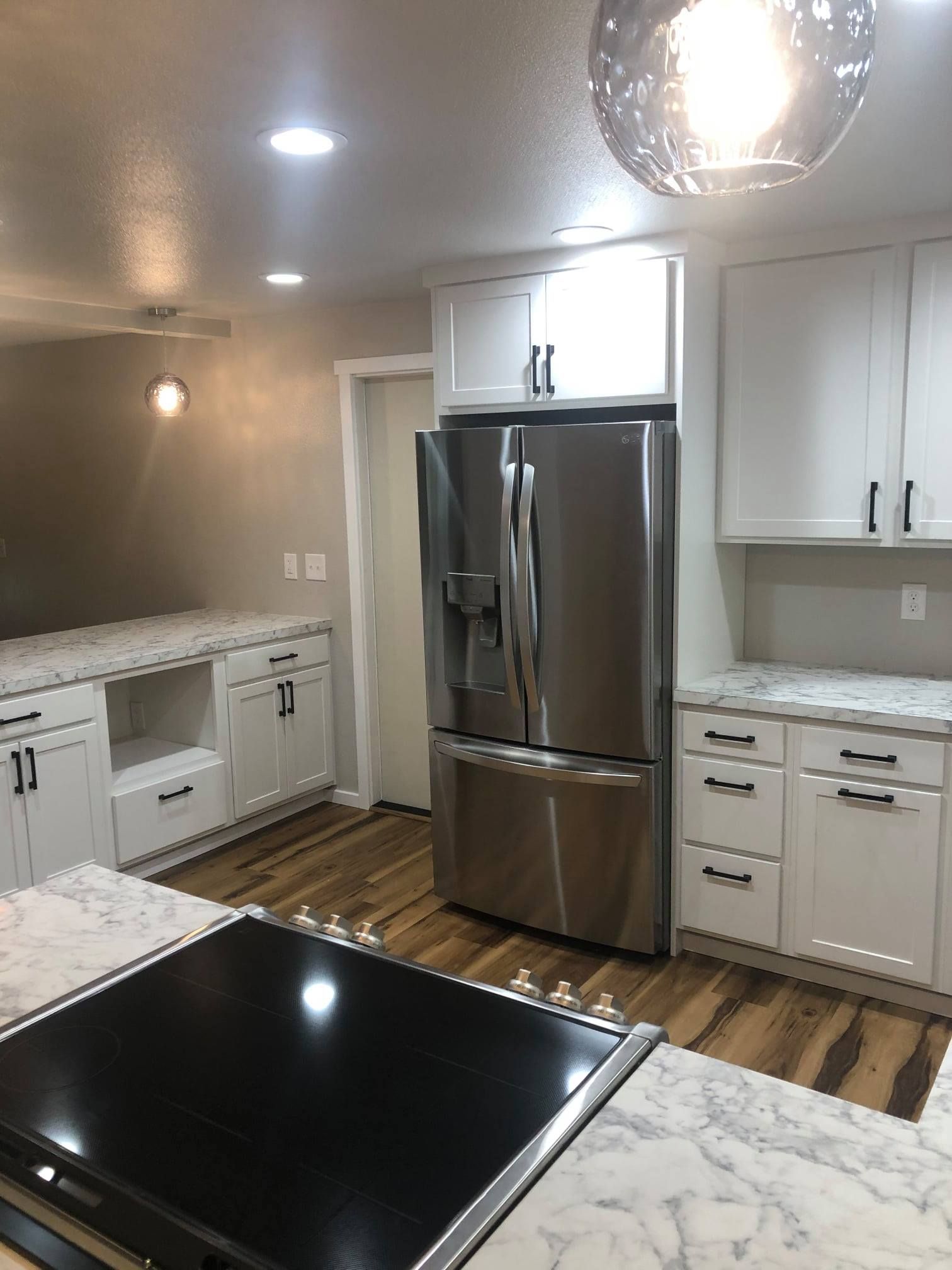 Modern kitchen with white cabinets, stainless steel refrigerator, and marble countertops.