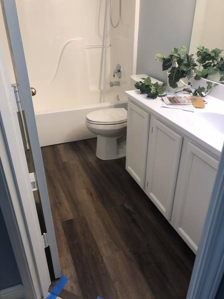Bathroom with new brown wood-look flooring, white vanity, toilet, and bathtub/shower.