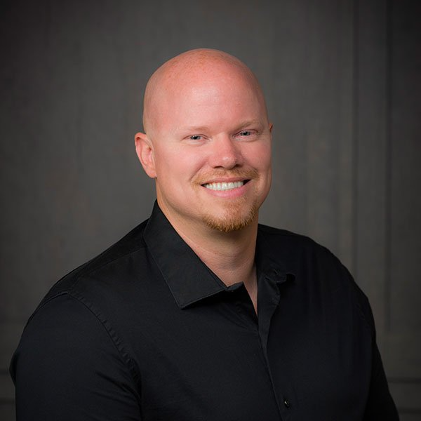 A bald man with a beard is wearing a black shirt and smiling for the camera.