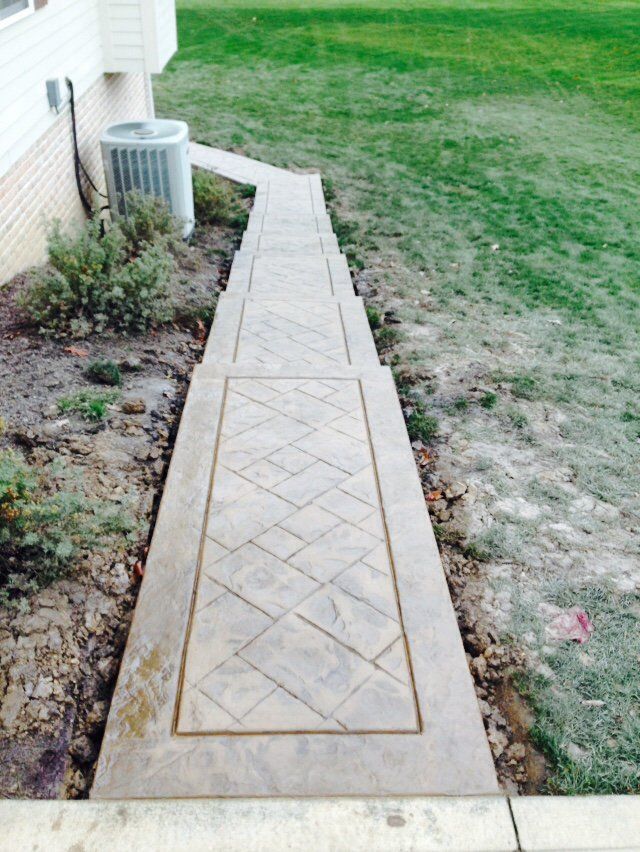 A concrete walkway leading to a house with a lawn in the background.