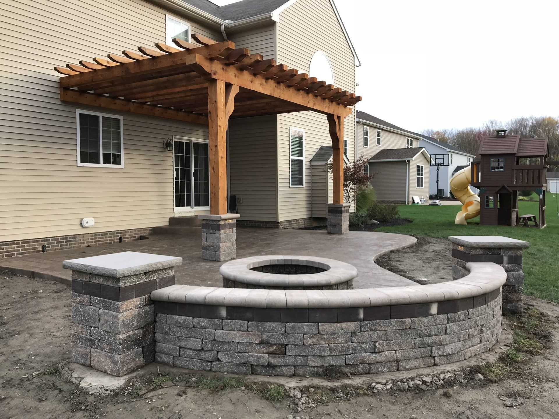 A patio with a fire pit and a pergola in front of a house.