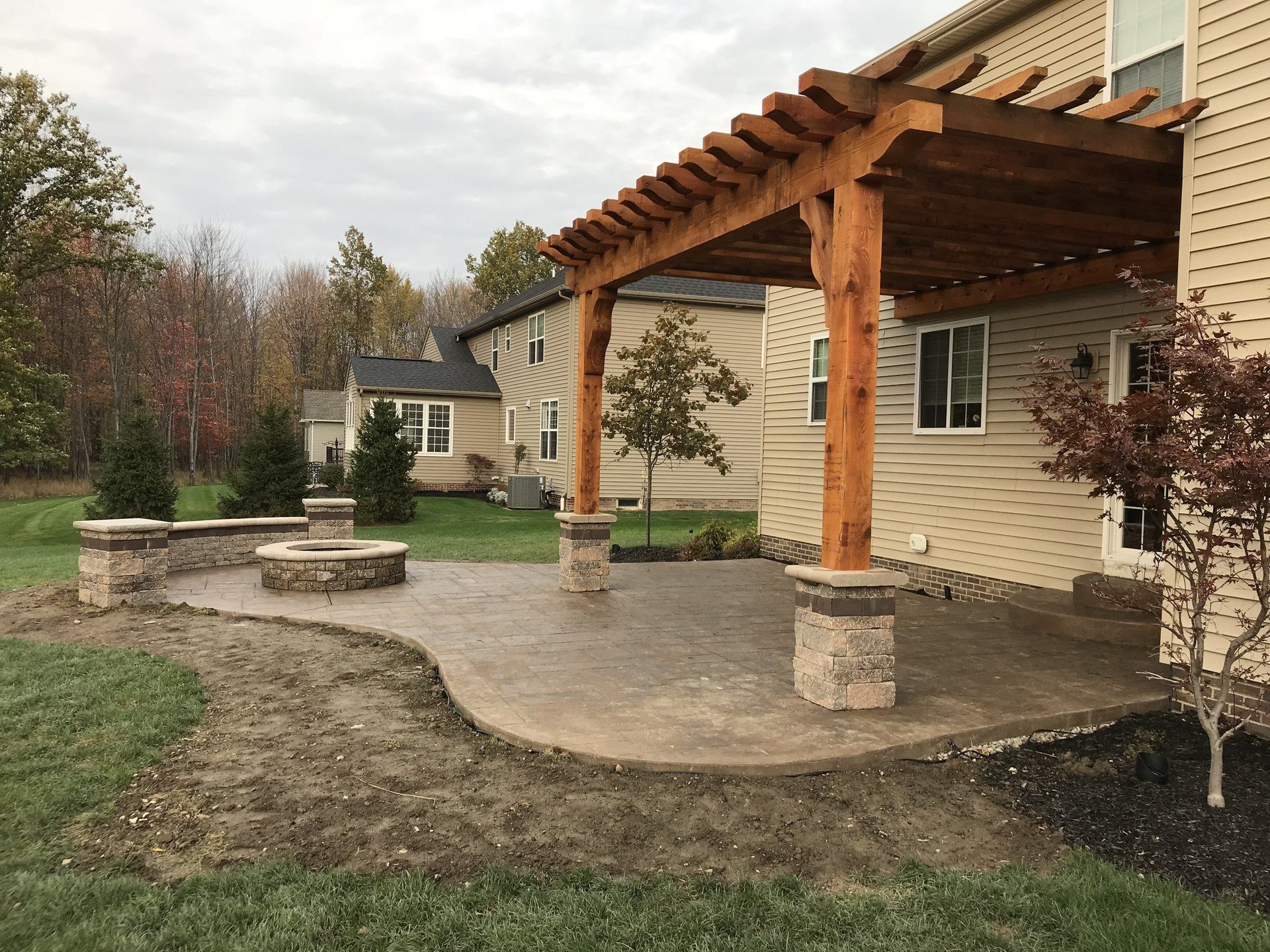 A patio with a pergola and a fire pit in front of a house.