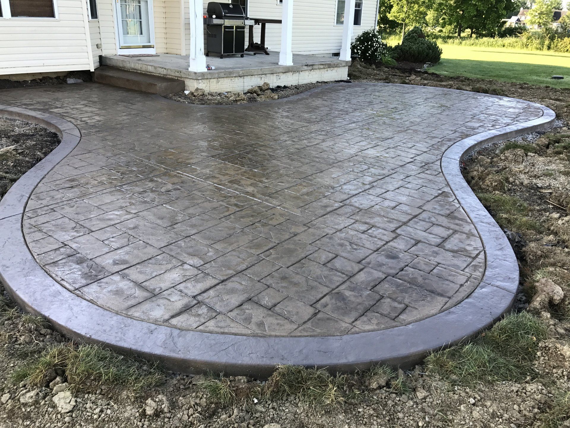 A concrete patio with a curved border is in front of a house.