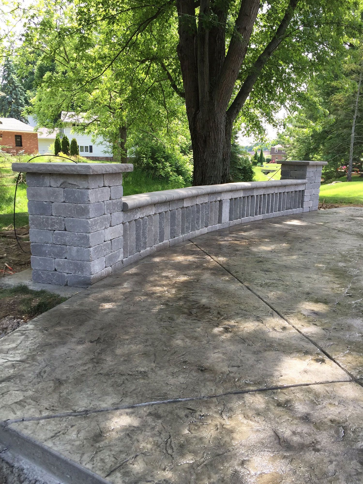 A stone wall with a tree in the background and a house in the background.