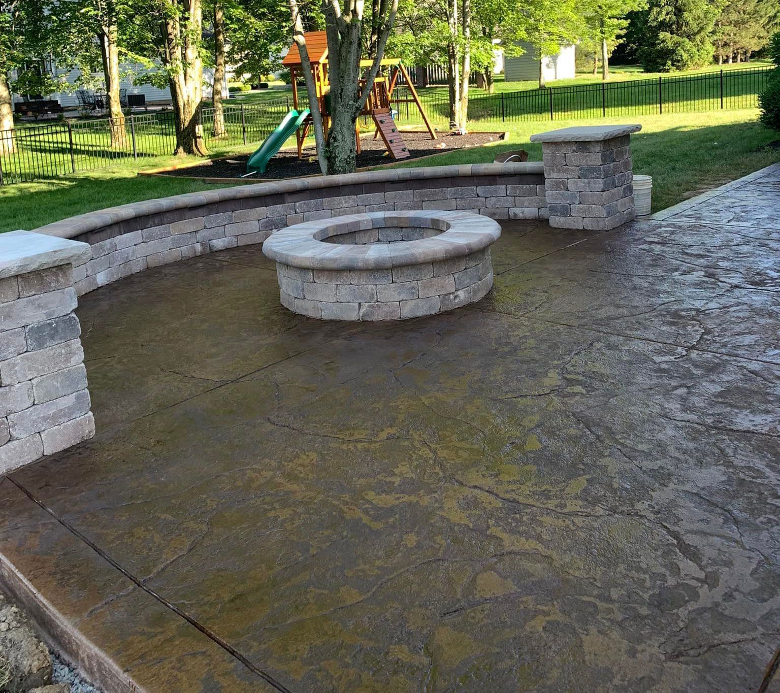 A fire pit in the middle of a patio with a playground in the background