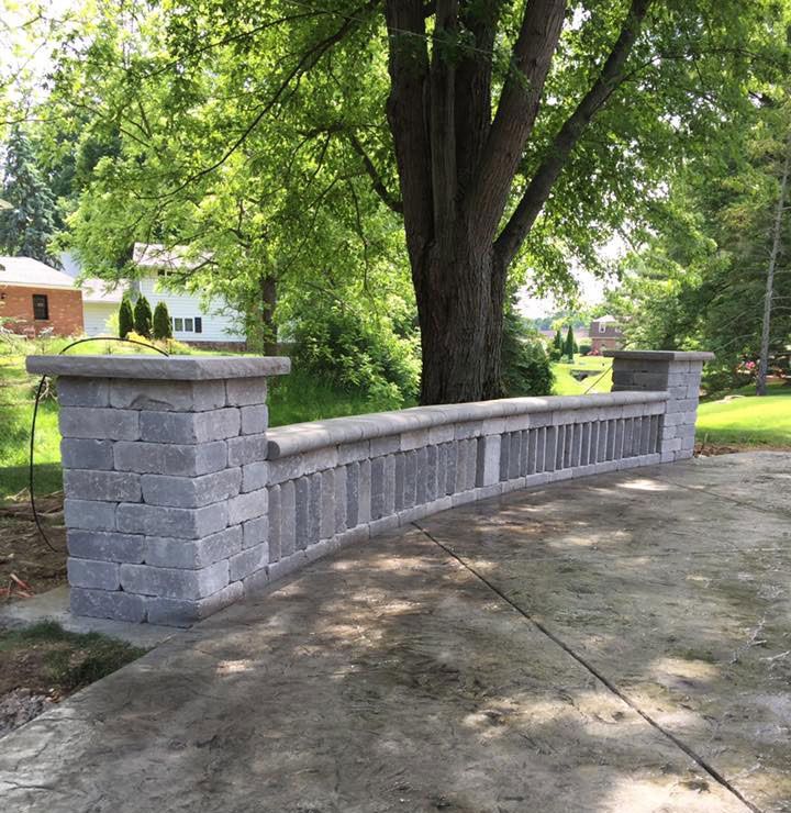 A stone wall with a tree in the background and a house in the background