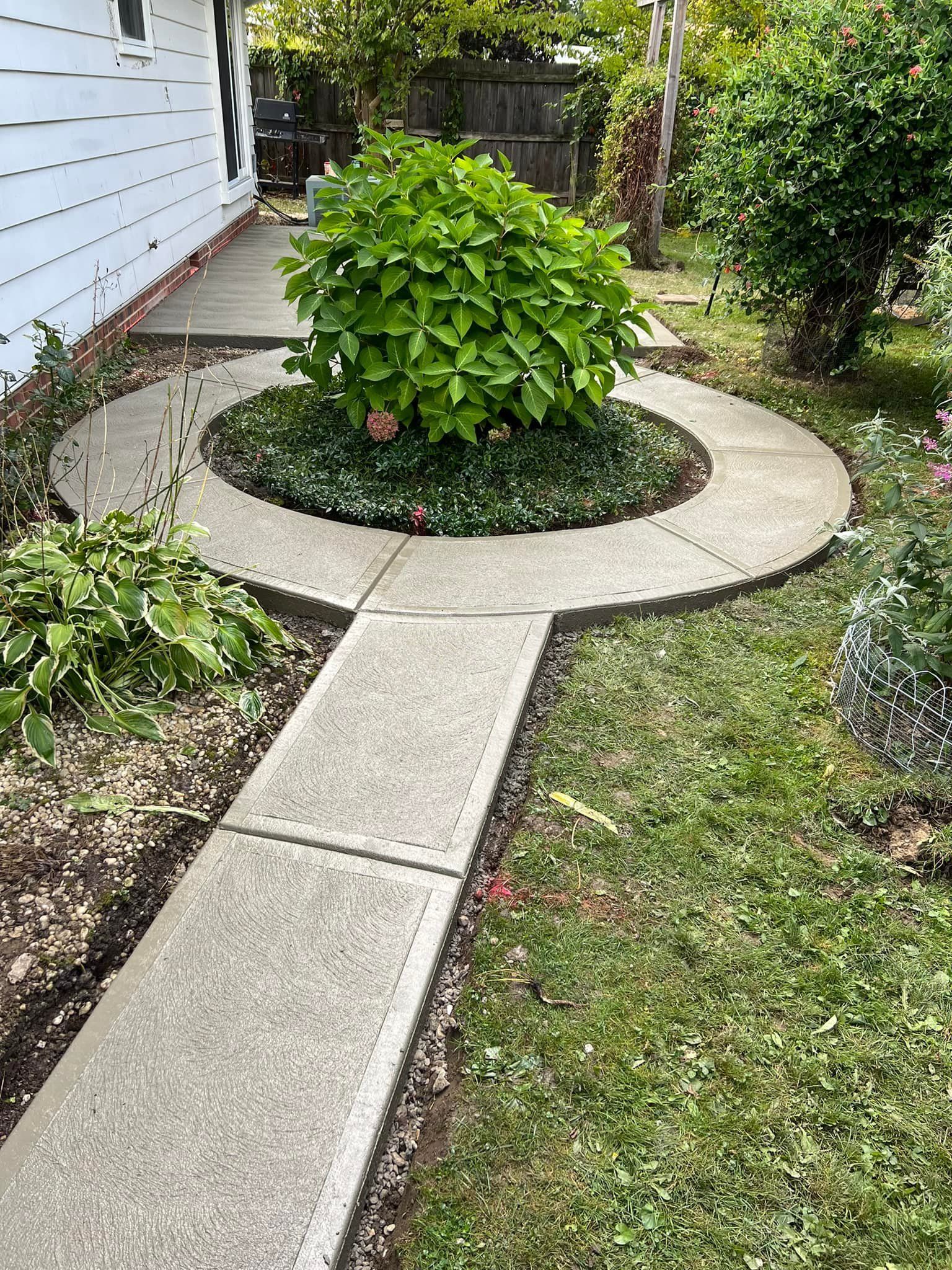 A concrete walkway leading to a house with a bush in the middle.