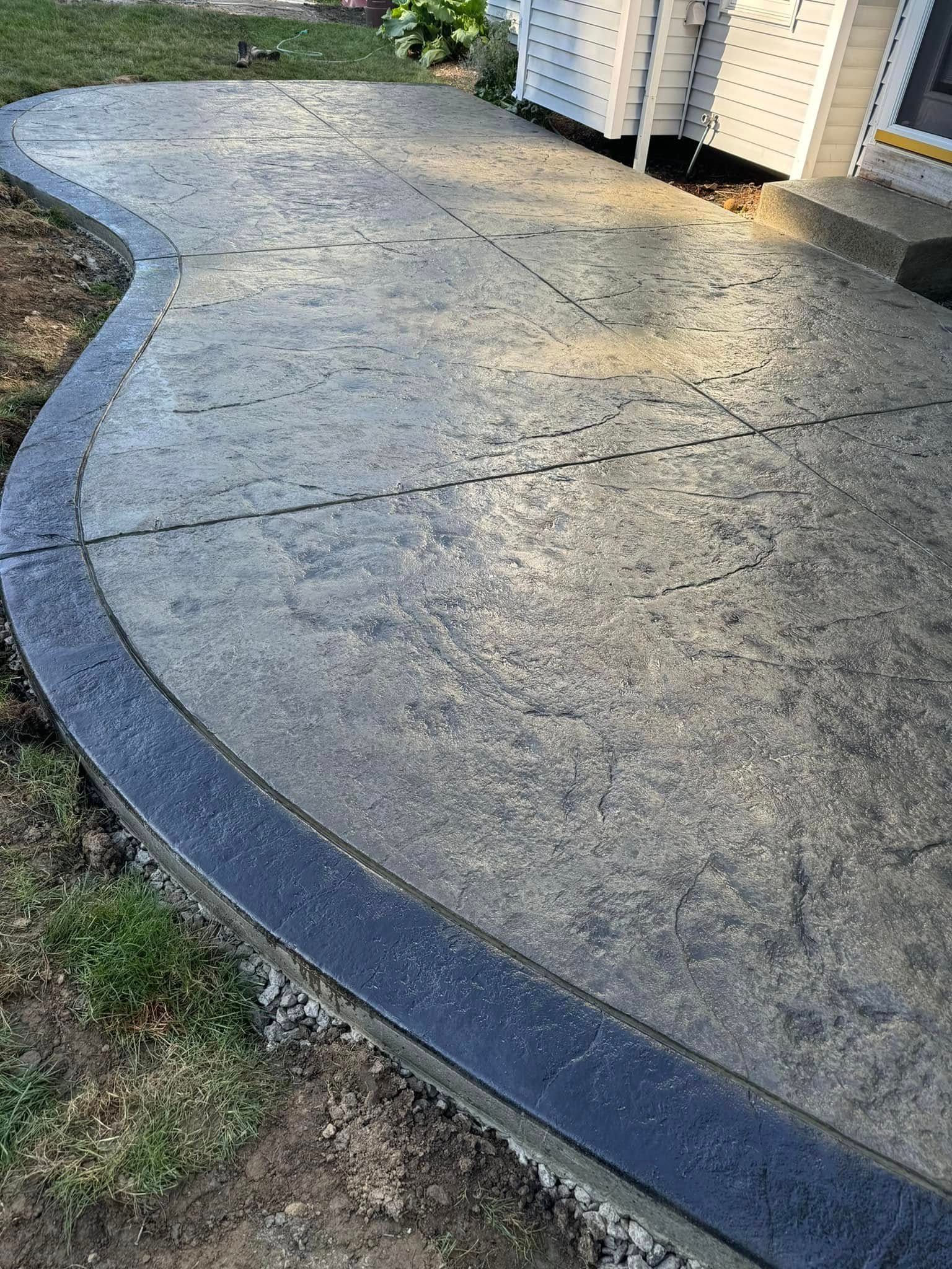 A concrete walkway with a black border is being built in front of a house.