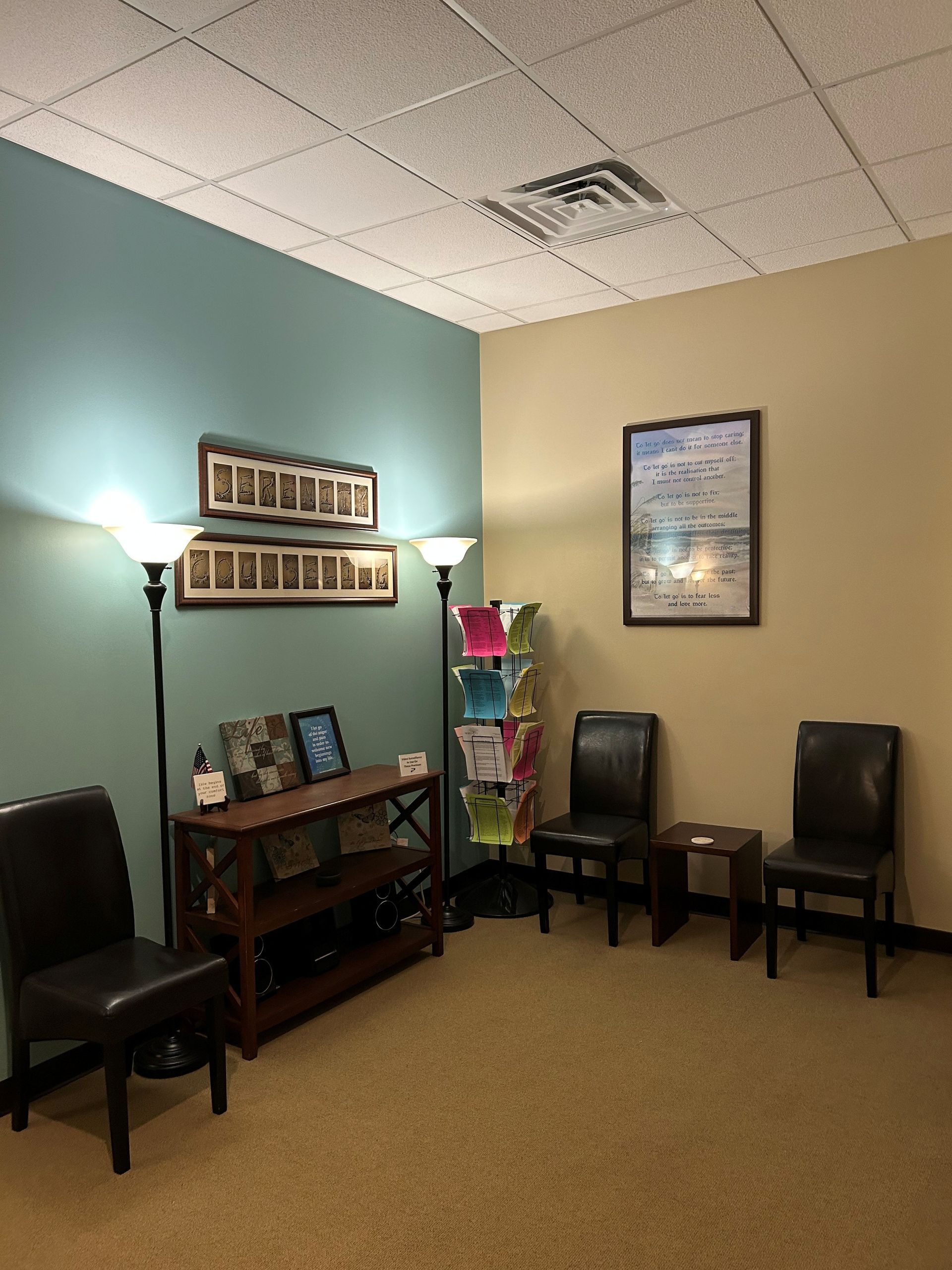 A waiting room with chairs a table and a lamp.