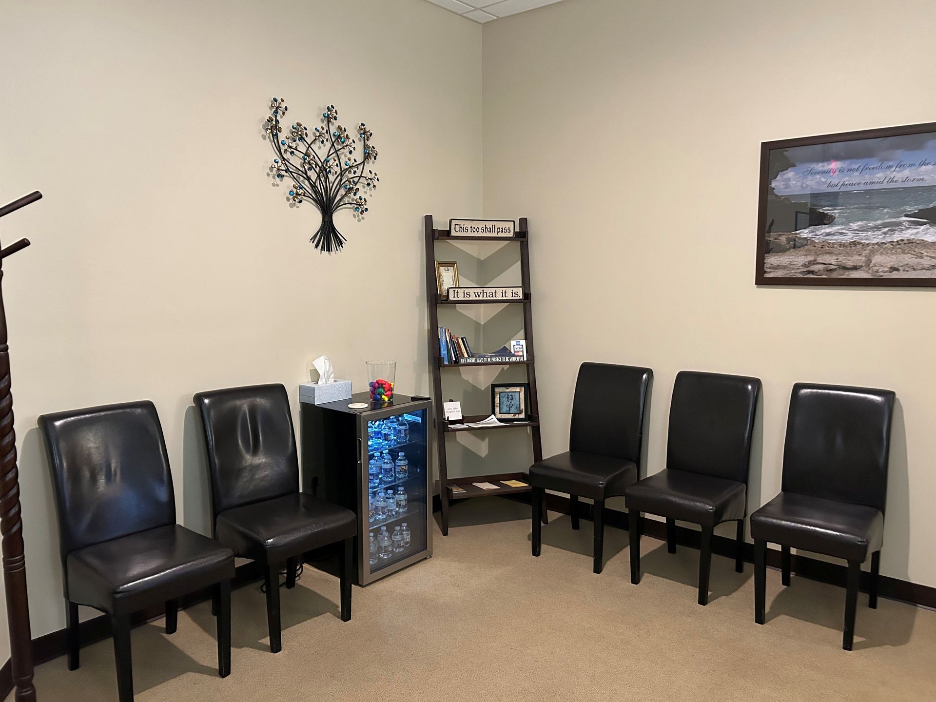 A waiting room with black chairs and a picture on the wall.