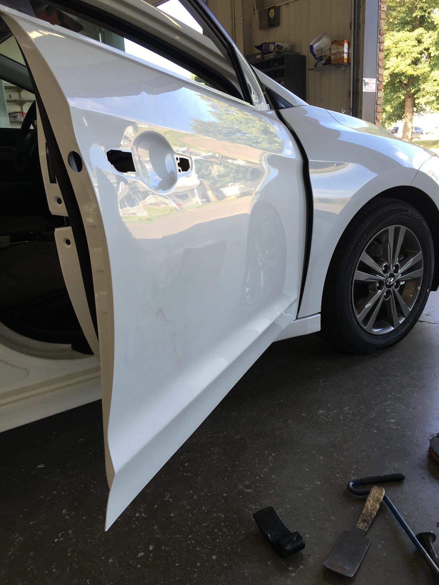 White car with open door in a repair shop. Door panel detached.