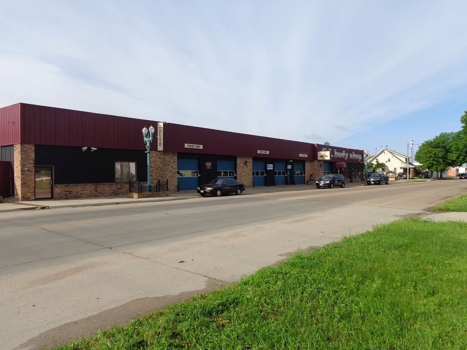Auto repair shop with red roof and blue garage doors on a city street. Cars parked out front.