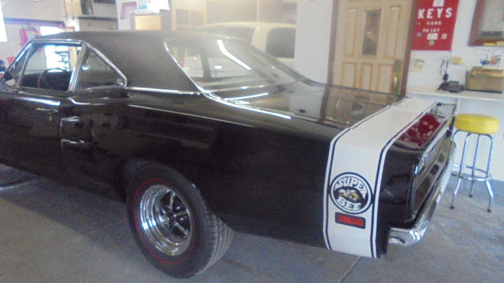 Black classic car with white racing stripe and logo in a garage.