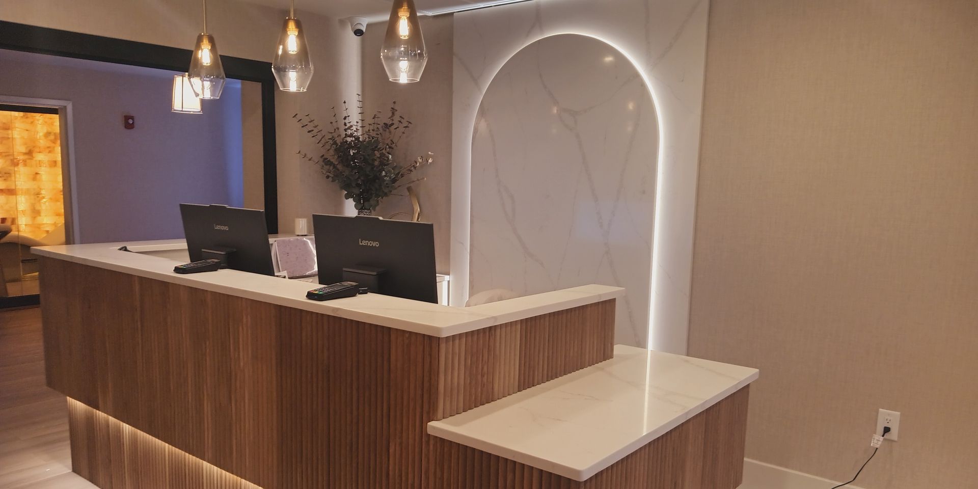 Reception desk in a spa or office, with computers, wood paneling, and a glowing arch.