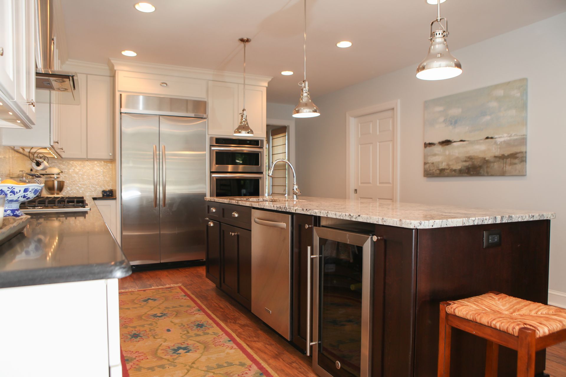 Kitchen with stainless steel appliances, dark island with wine fridge, and light blue walls.