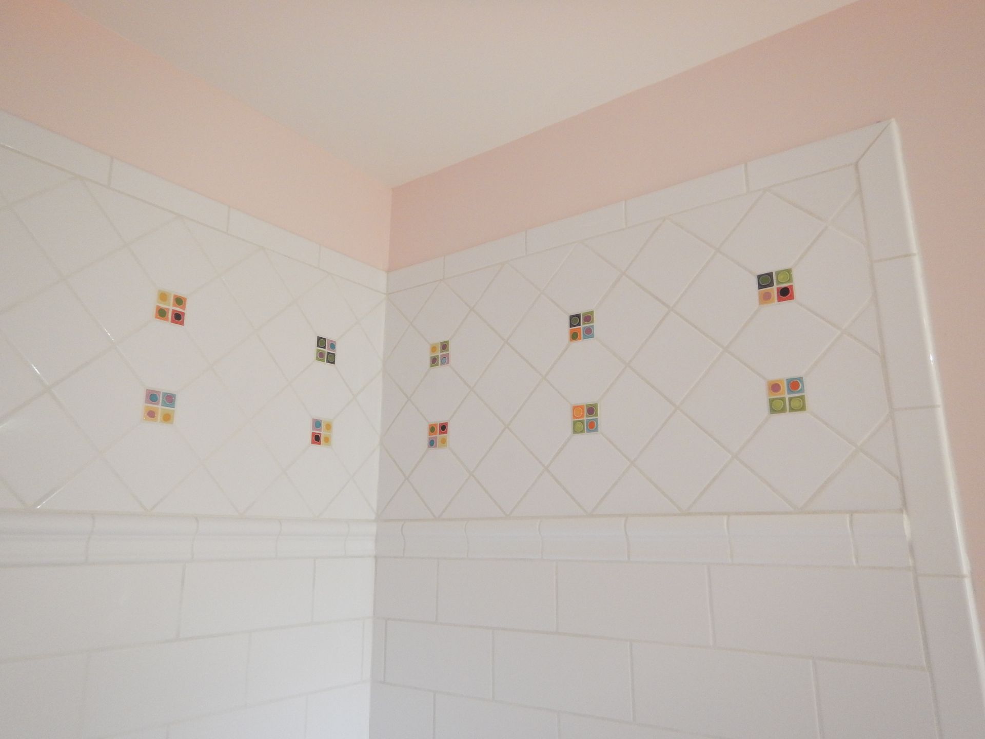 White tiled bathroom walls with square decorative tiles; pink ceiling.