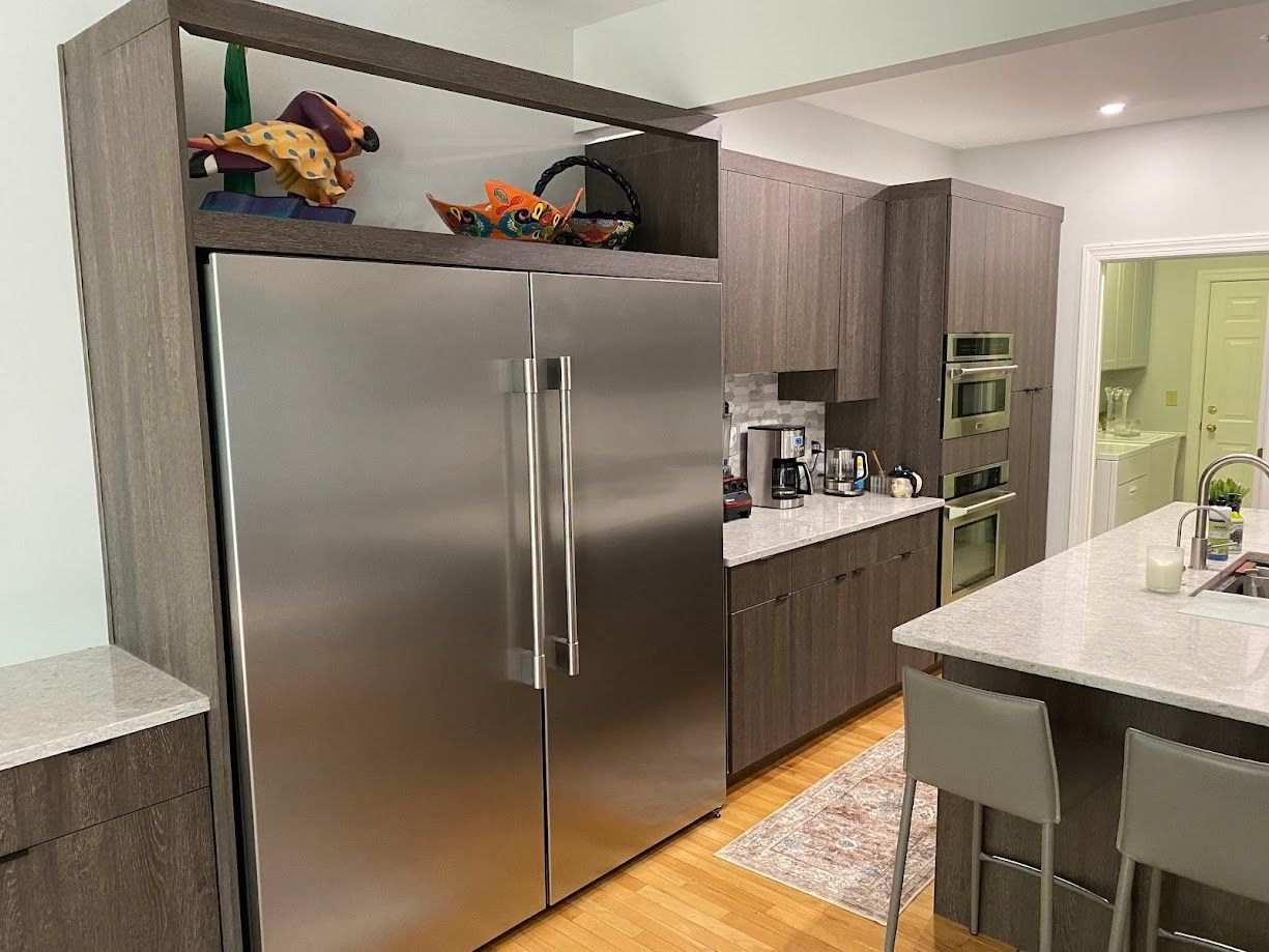 Stainless steel refrigerator built into gray cabinets in a kitchen with an island.