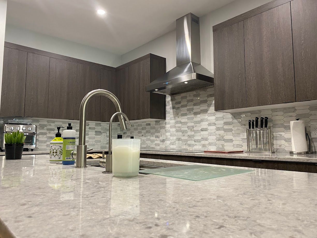 Modern kitchen with gray cabinets, stainless steel range hood, and light-colored countertop.