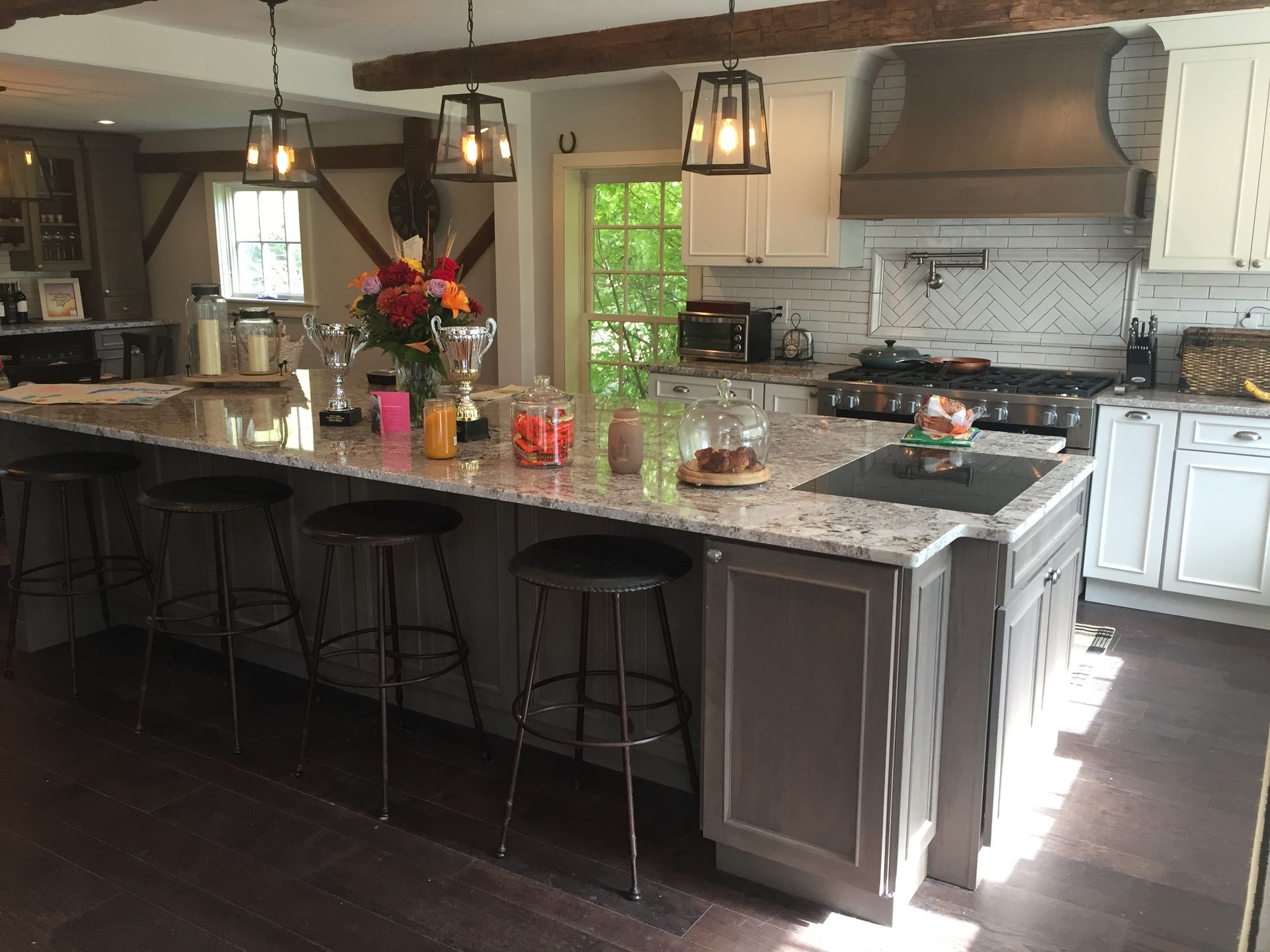 Kitchen with gray island, granite countertop, stools, overhead lights, stainless range, and white cabinetry.