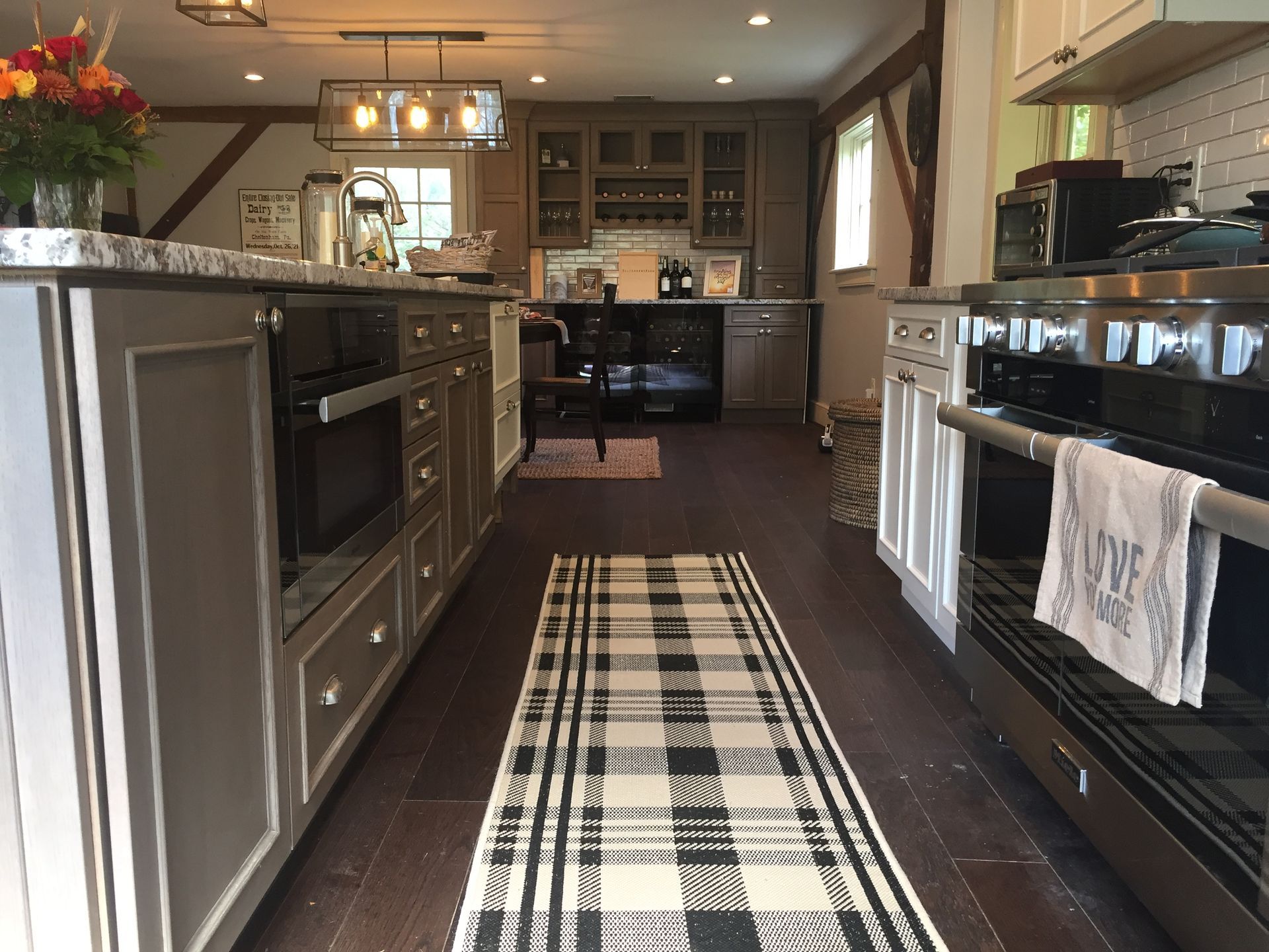 Kitchen with gray cabinets, stainless steel appliances, plaid rug, and dark wood floor.