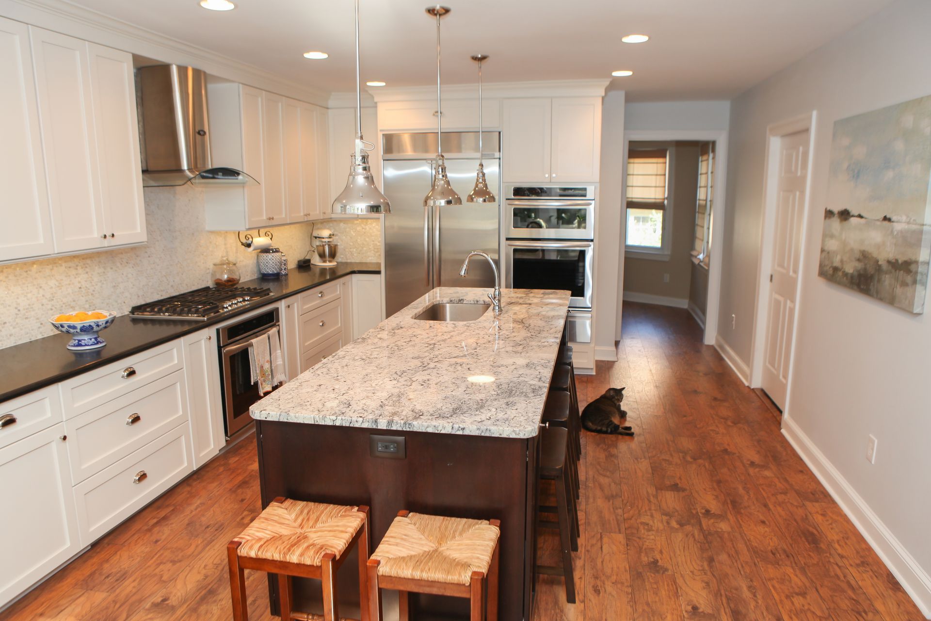 Modern kitchen with white cabinets, dark countertops, and a granite island with stools; a dog lies on the hardwood floor.
