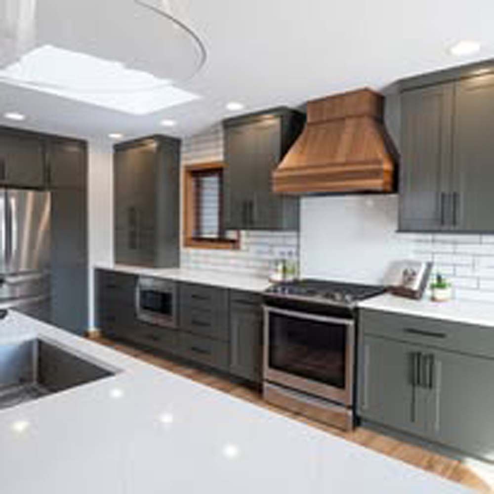 Modern kitchen with dark gray cabinets, white countertops, and wooden hood.