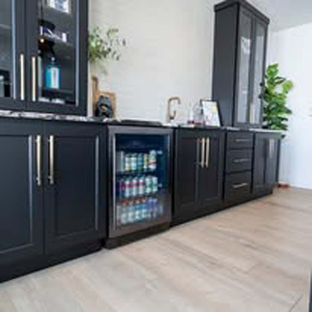 Dark cabinetry with a built-in beverage cooler, sink, and tall storage cabinet in a bright room.