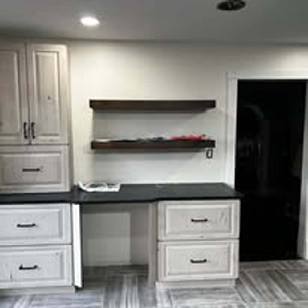 Built-in white desk with cabinets, drawers, and shelving; black door and hardwood floors.