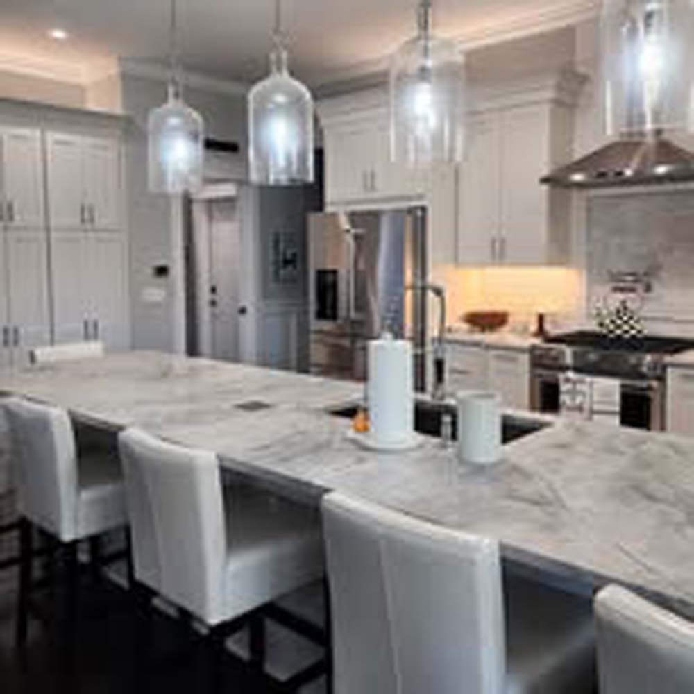Kitchen with marble countertop island, white cabinets, and hanging pendant lights.