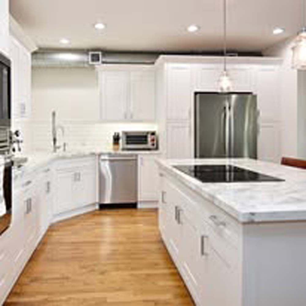 Modern white kitchen with stainless steel appliances, marble countertop island, and wood floors.
