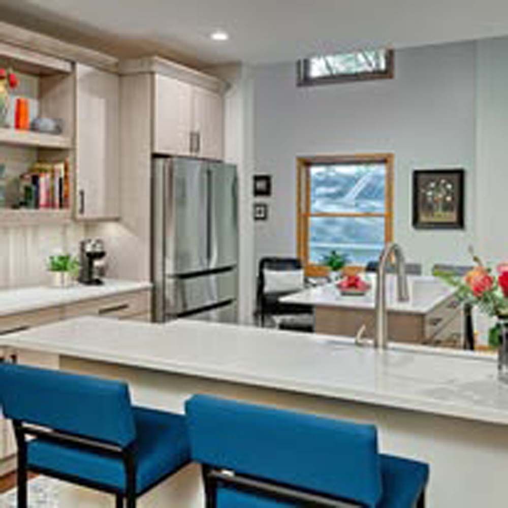 A modern kitchen with a white island, blue stools, stainless steel refrigerator, and wooden cabinets.