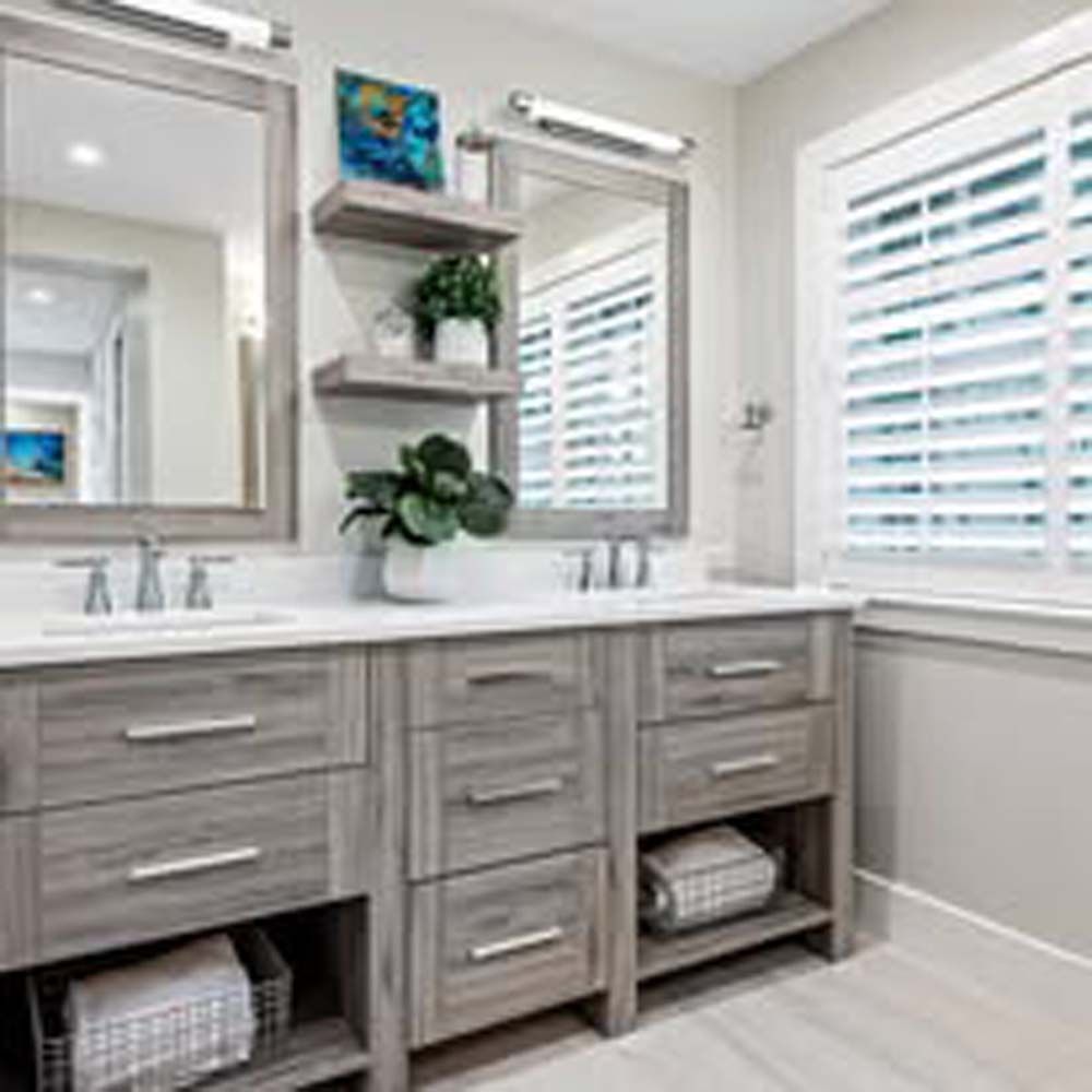 Bathroom with double vanity, mirrors, floating shelves, and window with shutters.