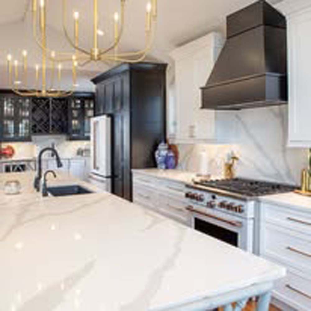 Modern kitchen with white countertops, black hood, and gold chandelier.