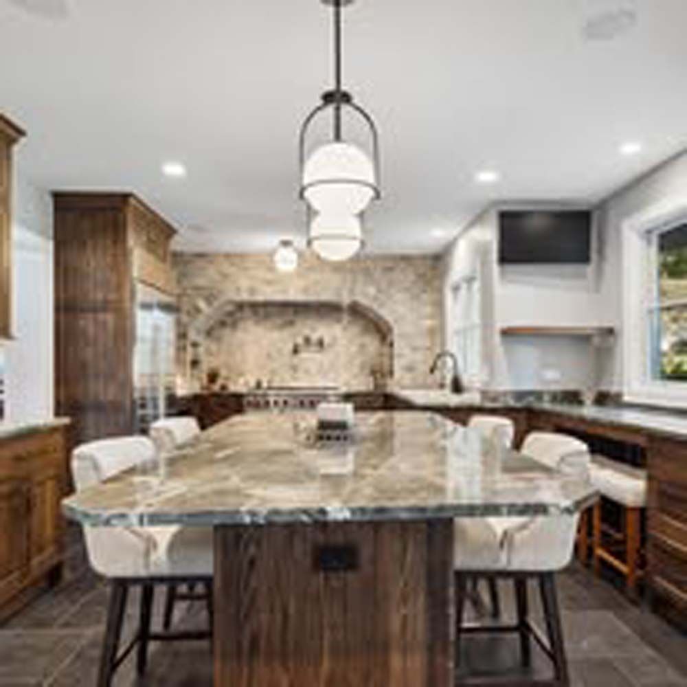 Kitchen with marble island, pendant lights, wooden cabinets, and stone backsplash.